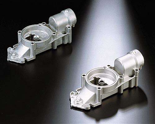 The image shows a pair of aluminum die casting parts on a black surface. The parts are silver in color and have a glossy finish. They are arranged in a symmetrical pattern, with each part slightly ove